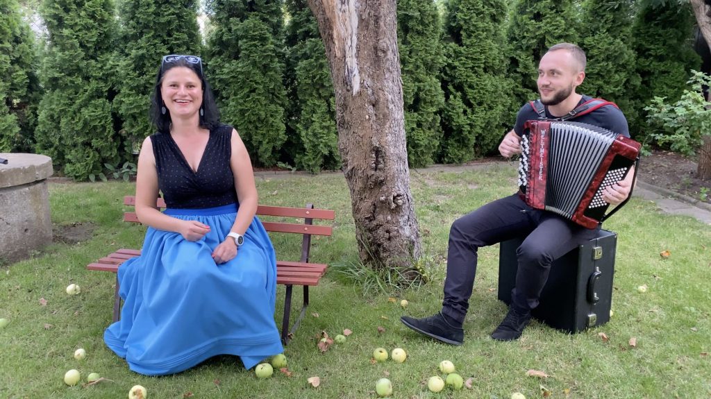 . Para muzyków siedzi w ogrodzie pod jabłonią